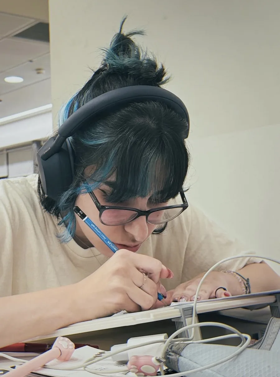 Sarah Araide drawing with a pencil at her desk, wearing headphones
